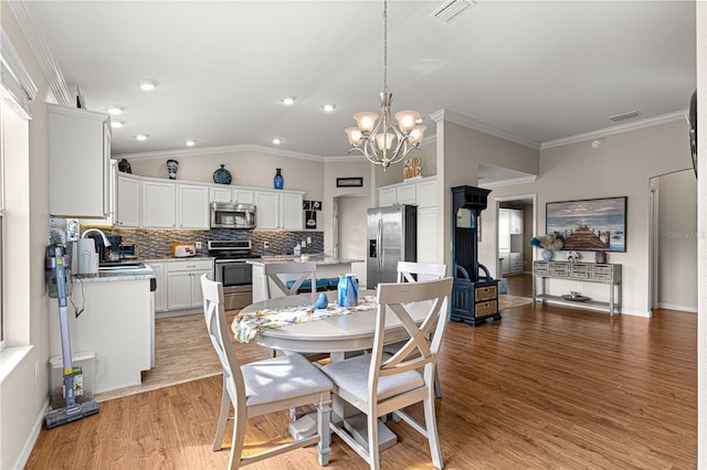 dining room with sink, vaulted ceiling, ornamental molding, a notable chandelier, and hardwood / wood-style flooring