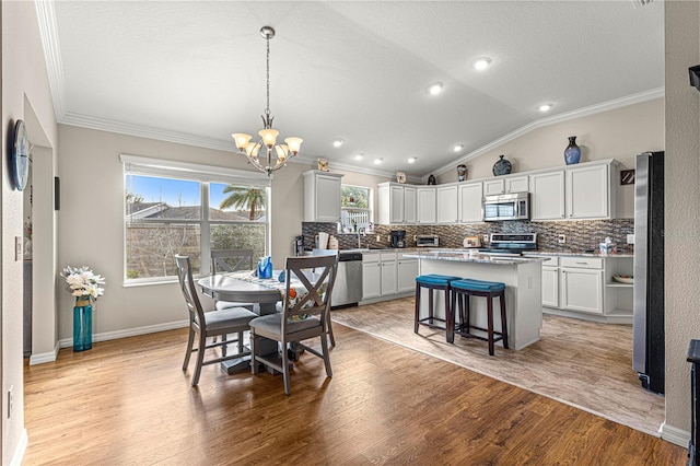 dining room featuring lofted ceiling, light hardwood / wood-style flooring, an inviting chandelier, ornamental molding, and a textured ceiling