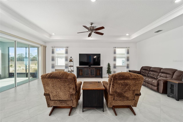 tiled living room with ceiling fan, a raised ceiling, and a wealth of natural light