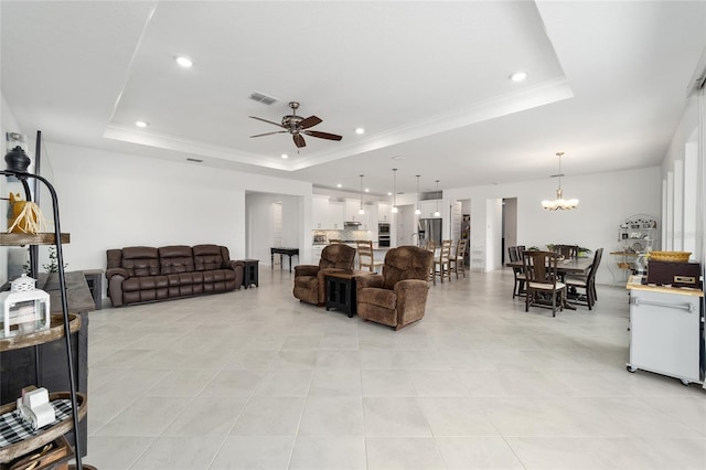 tiled living room featuring a raised ceiling, ornamental molding, and ceiling fan with notable chandelier