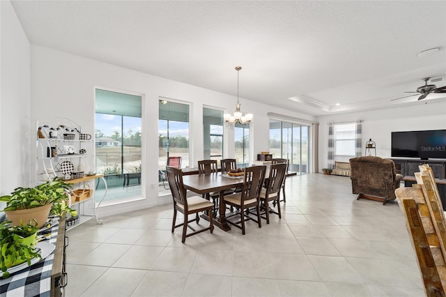 tiled dining area featuring a tray ceiling, ceiling fan with notable chandelier, and a textured ceiling