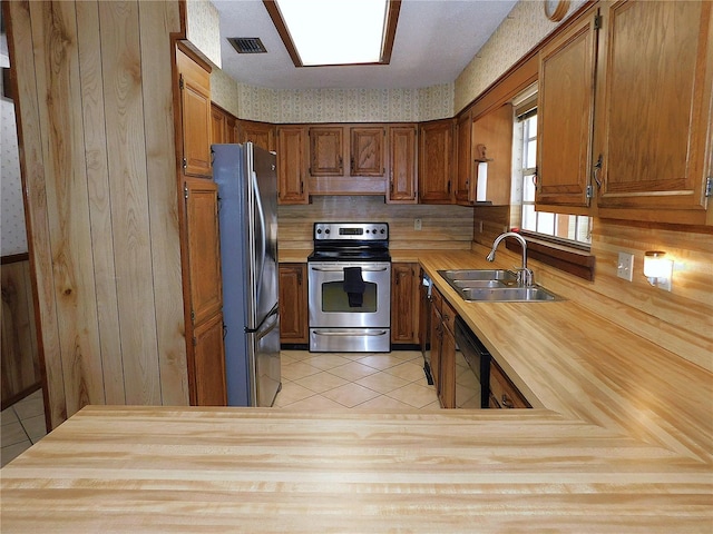 kitchen with appliances with stainless steel finishes, sink, light tile patterned floors, and wooden walls