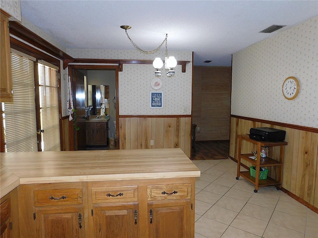 kitchen featuring light tile patterned flooring, pendant lighting, wood counters, a notable chandelier, and kitchen peninsula