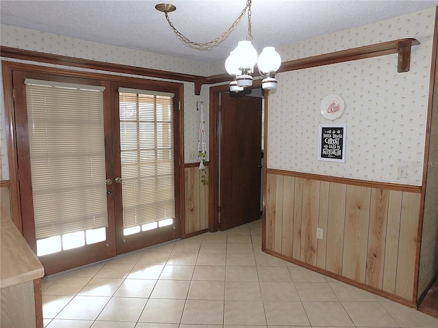 unfurnished dining area with french doors, light tile patterned flooring, an inviting chandelier, a textured ceiling, and wooden walls