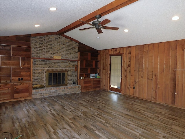 unfurnished living room with a fireplace, lofted ceiling with beams, wooden walls, and a textured ceiling