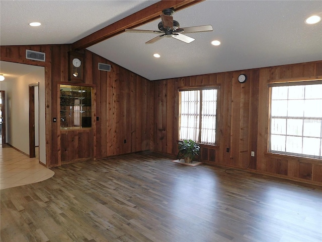 unfurnished living room featuring dark hardwood / wood-style floors, wooden walls, lofted ceiling with beams, ceiling fan, and a textured ceiling