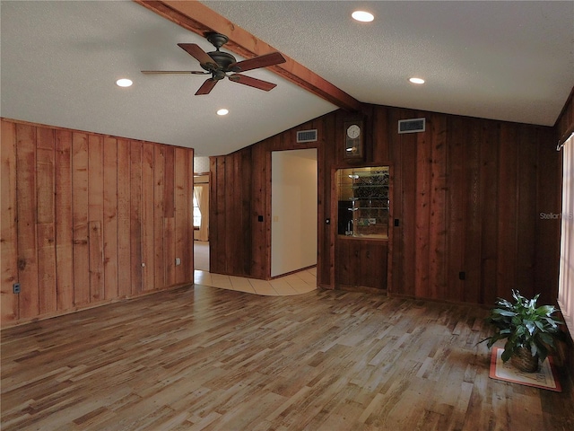 unfurnished living room with ceiling fan, vaulted ceiling with beams, light hardwood / wood-style floors, a textured ceiling, and wood walls