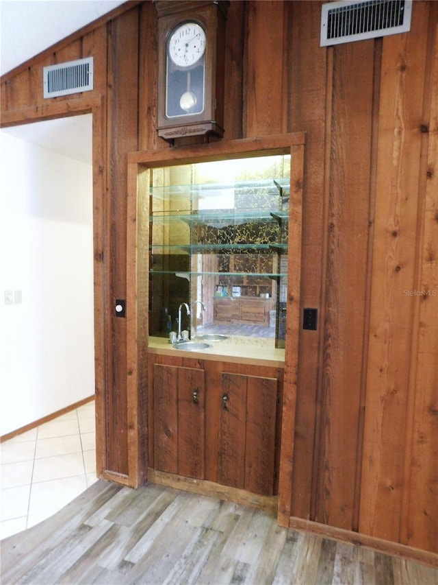 bar featuring sink, light hardwood / wood-style floors, and wood walls