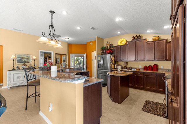 kitchen featuring lofted ceiling, sink, a breakfast bar area, a center island with sink, and stainless steel fridge with ice dispenser