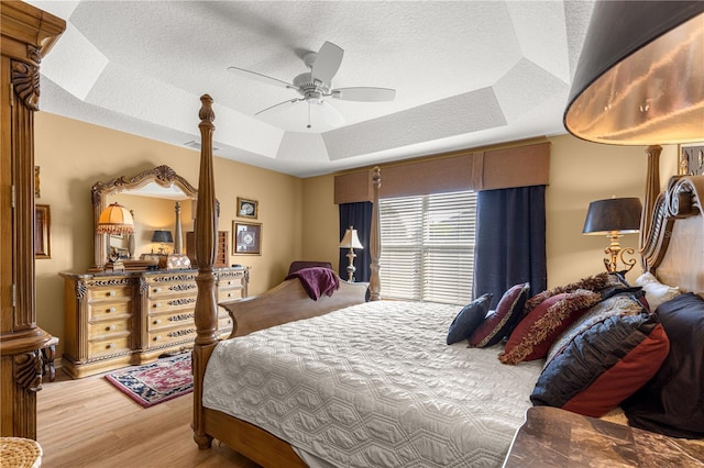 bedroom with ceiling fan, hardwood / wood-style floors, a textured ceiling, and a tray ceiling