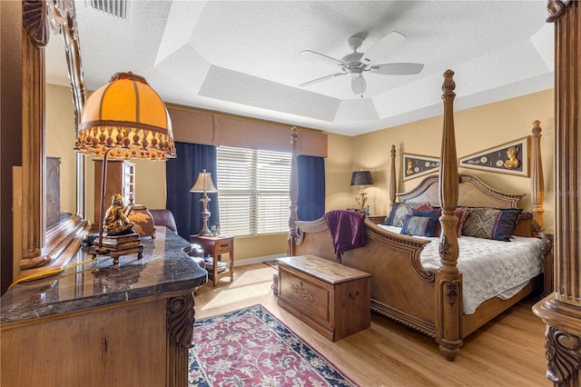 bedroom featuring ceiling fan, a raised ceiling, a textured ceiling, and light wood-type flooring