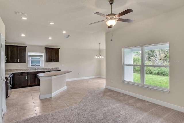 kitchen with stainless steel range oven, light stone counters, ceiling fan with notable chandelier, light tile patterned floors, and sink