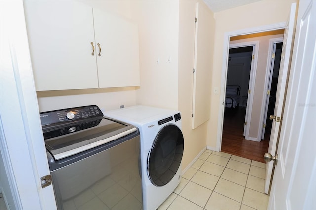 clothes washing area with light tile patterned floors, washer and clothes dryer, and cabinets