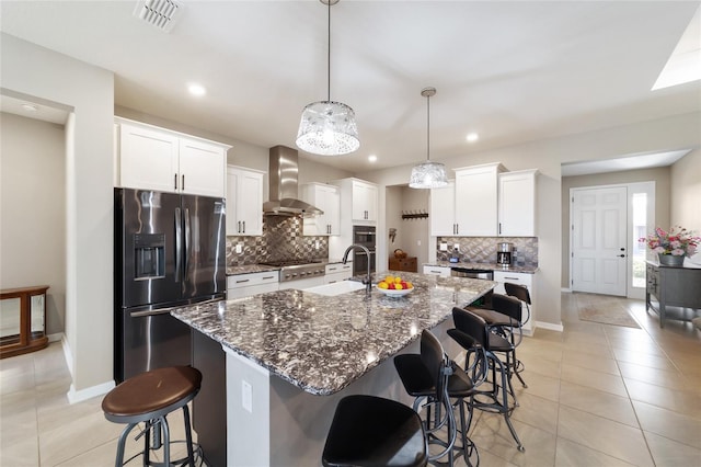 kitchen featuring pendant lighting, white cabinets, a kitchen island with sink, stainless steel appliances, and wall chimney exhaust hood