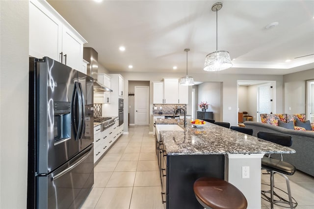 kitchen with stainless steel appliances, tasteful backsplash, a center island with sink, and wall chimney range hood