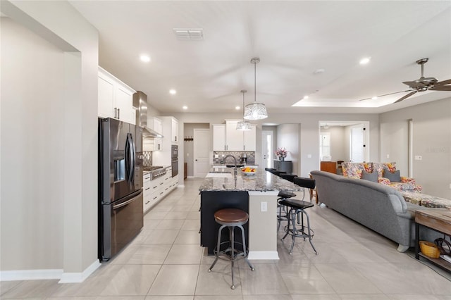 kitchen featuring wall chimney exhaust hood, stainless steel appliances, an island with sink, and white cabinets