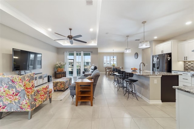 living room with ceiling fan, a tray ceiling, and light tile patterned floors