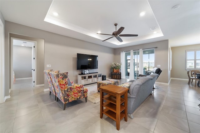 living room featuring a wealth of natural light, ceiling fan, and a tray ceiling