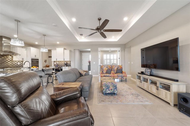 living room featuring light tile patterned flooring, sink, ornamental molding, ceiling fan, and a tray ceiling