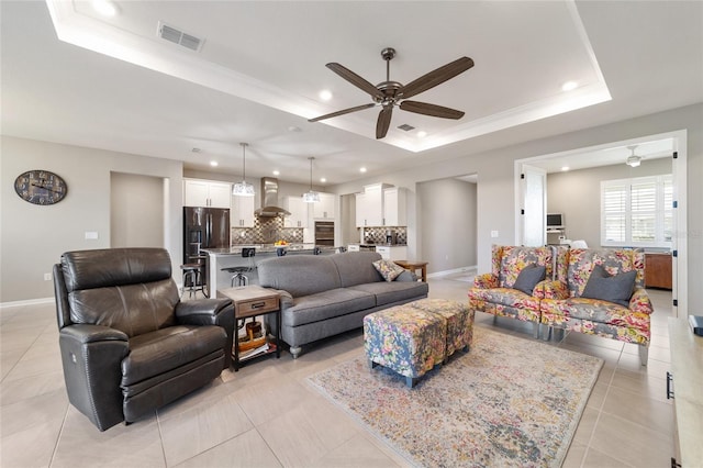 living room featuring a raised ceiling, light tile patterned flooring, and ceiling fan