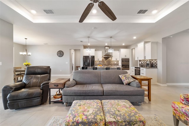 living room featuring a tray ceiling, light tile patterned floors, ceiling fan with notable chandelier, and ornamental molding