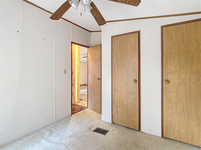 unfurnished bedroom with crown molding, light colored carpet, ceiling fan, and two closets