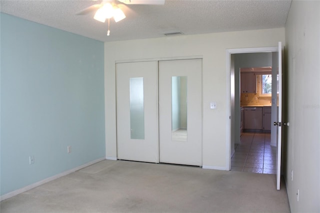 unfurnished bedroom featuring ceiling fan, a closet, light carpet, and a textured ceiling