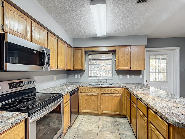 kitchen with brown cabinets, appliances with stainless steel finishes, a sink, light stone countertops, and a peninsula