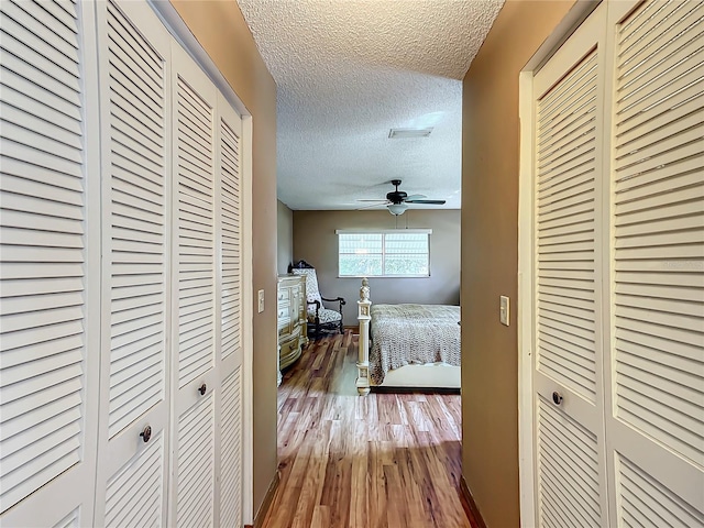 hall with a textured ceiling, wood finished floors, and visible vents