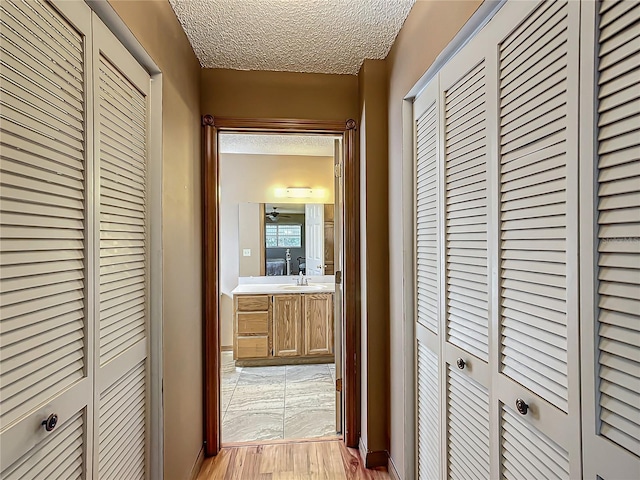 hall featuring a textured ceiling, a sink, and light wood-style floors