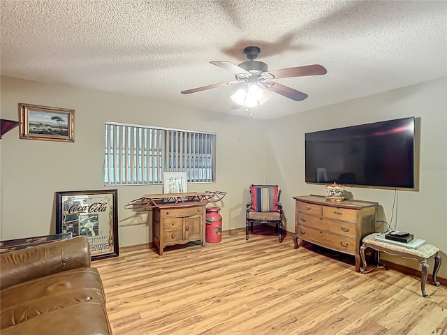 living room featuring ceiling fan, light wood finished floors, and a textured ceiling