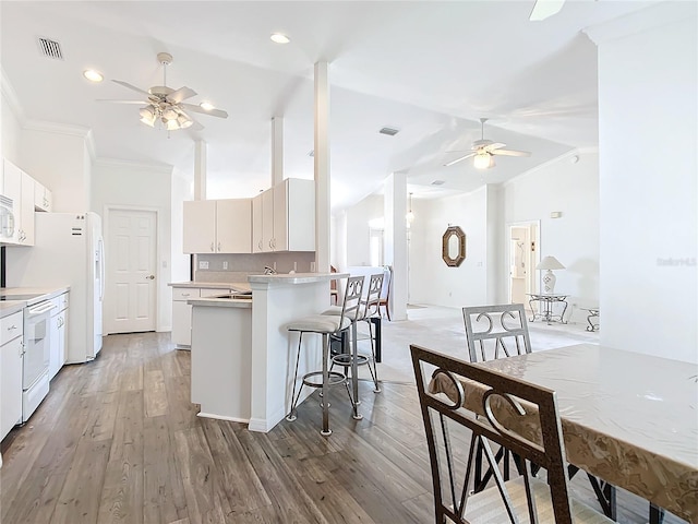 kitchen with lofted ceiling, white appliances, hardwood / wood-style flooring, ornamental molding, and white cabinets