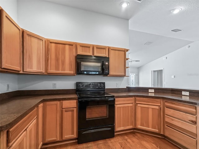 kitchen featuring light wood-type flooring, dark stone counters, vaulted ceiling, and black appliances