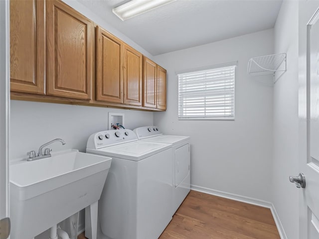 clothes washing area featuring cabinets, sink, washing machine and clothes dryer, and light wood-type flooring