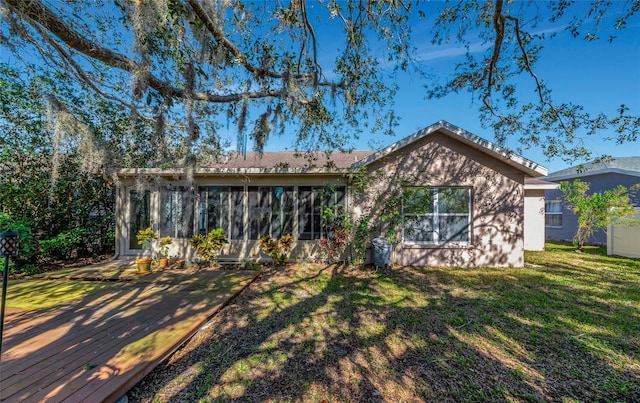 rear view of property with a yard, a deck, and a sunroom