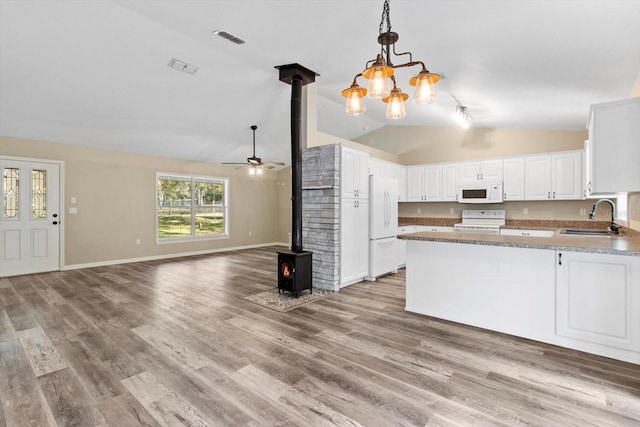 kitchen featuring sink, hanging light fixtures, a wood stove, white appliances, and white cabinets