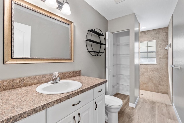 bathroom featuring hardwood / wood-style flooring, tiled shower, vanity, and toilet