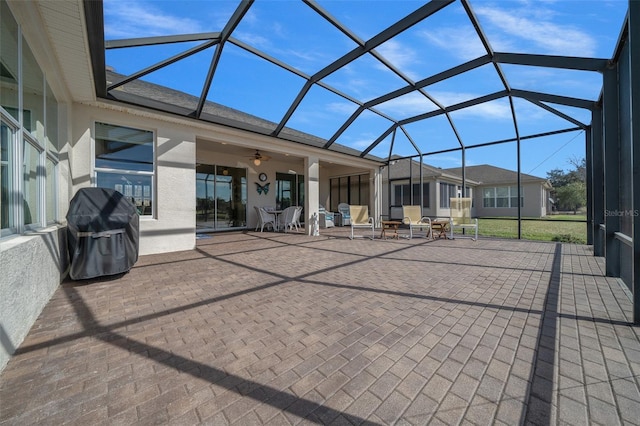 view of patio with ceiling fan, area for grilling, and glass enclosure