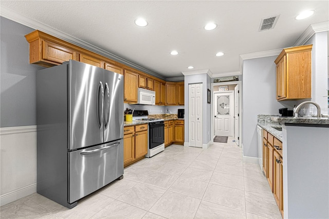 kitchen with gas range oven, ornamental molding, light stone countertops, and stainless steel refrigerator