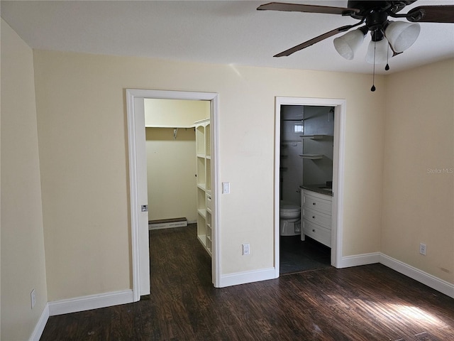 unfurnished bedroom featuring a spacious closet, baseboard heating, dark wood-type flooring, ensuite bath, and a closet