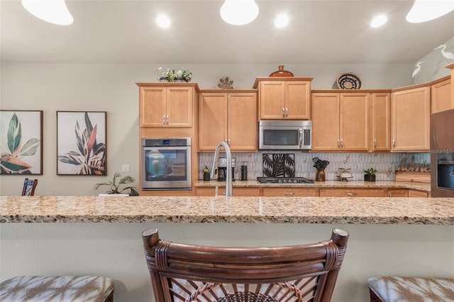 kitchen with a breakfast bar area, tasteful backsplash, light stone counters, hanging light fixtures, and appliances with stainless steel finishes