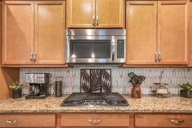 kitchen with stainless steel appliances, light stone countertops, and backsplash