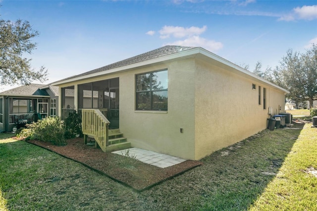 rear view of property with a sunroom, central AC, and a lawn