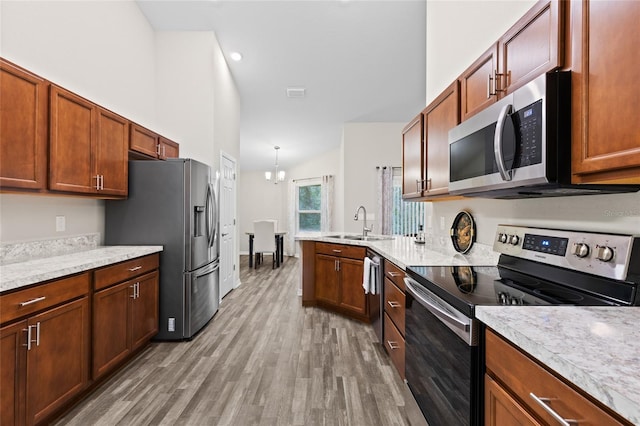 kitchen with sink, hanging light fixtures, stainless steel appliances, an inviting chandelier, and light hardwood / wood-style flooring