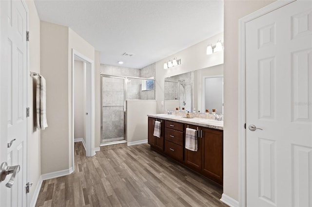 bathroom with vanity, wood-type flooring, a textured ceiling, and a shower with shower door