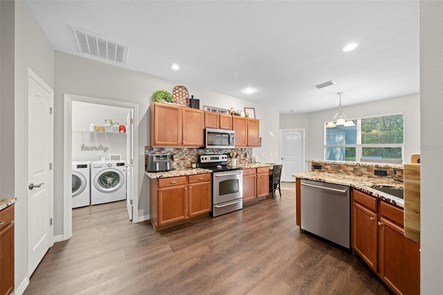 kitchen featuring hanging light fixtures, dark wood-type flooring, washer and clothes dryer, and appliances with stainless steel finishes