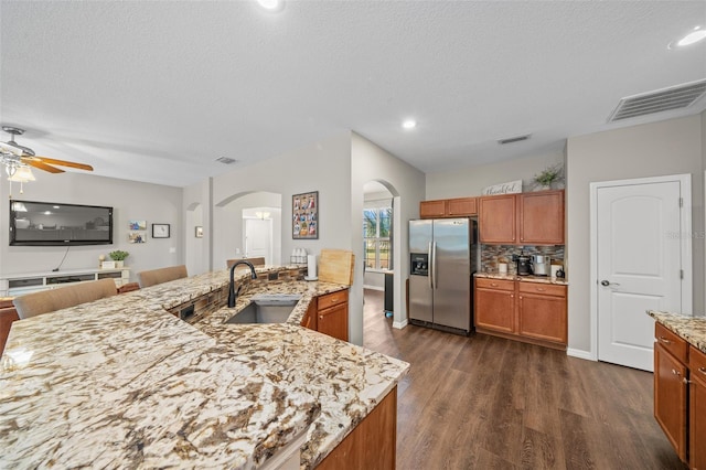 kitchen with tasteful backsplash, an island with sink, sink, stainless steel fridge, and dark wood-type flooring