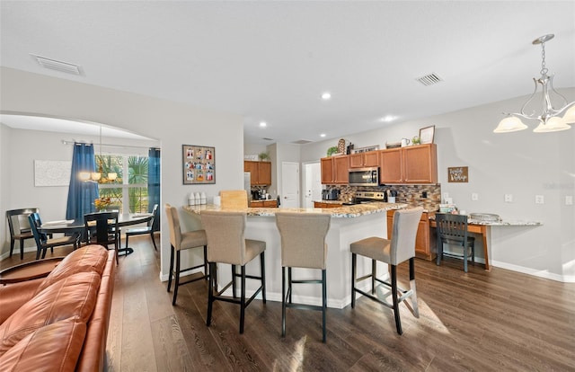 kitchen with appliances with stainless steel finishes, decorative light fixtures, a chandelier, kitchen peninsula, and dark wood-type flooring