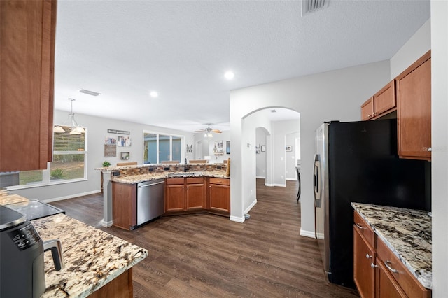 kitchen with appliances with stainless steel finishes, decorative light fixtures, sink, kitchen peninsula, and light stone countertops