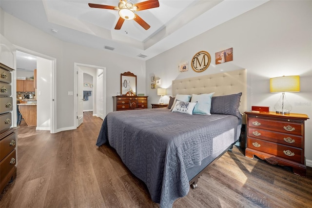 bedroom with a raised ceiling, hardwood / wood-style floors, and ceiling fan